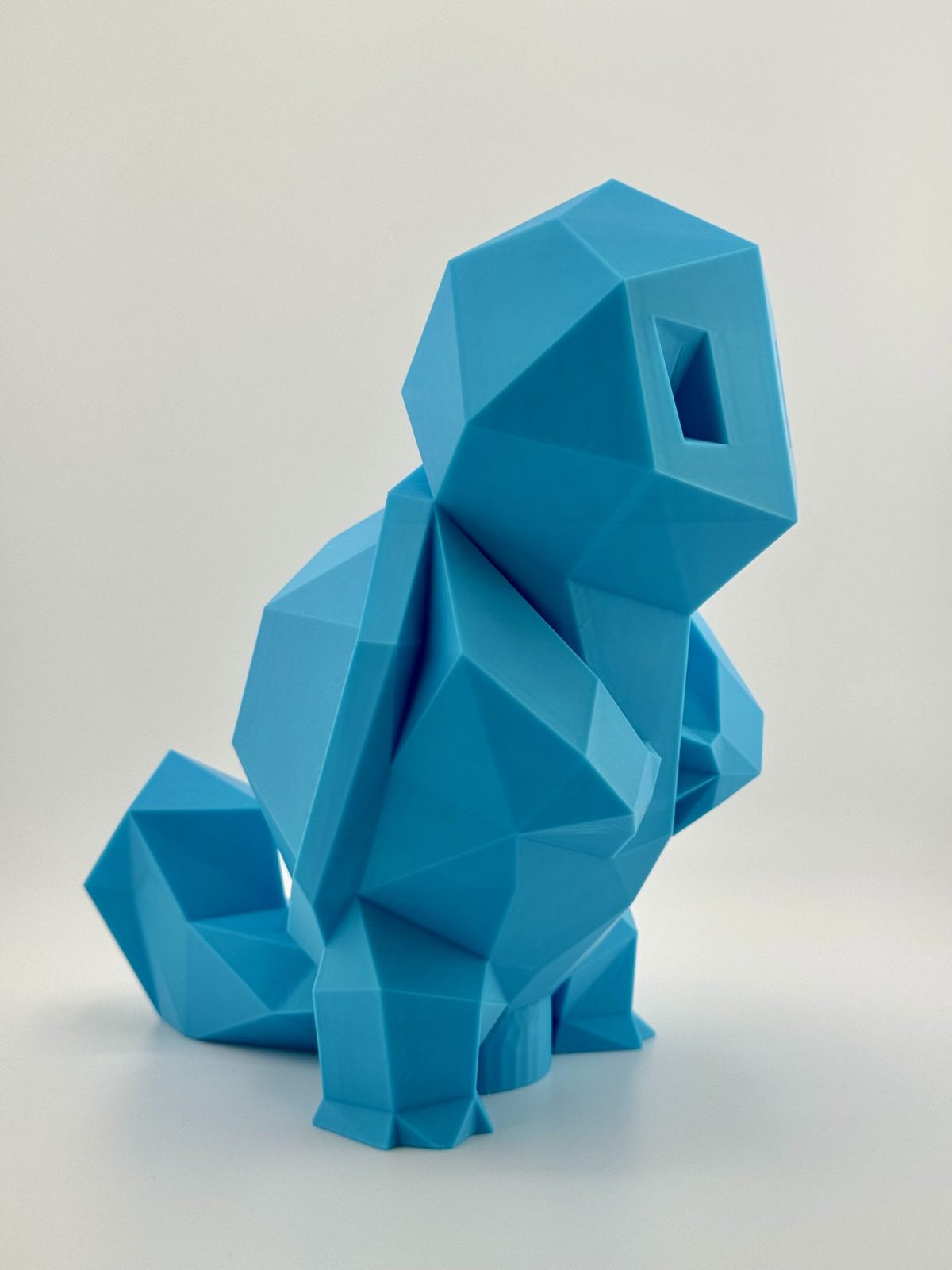 Light blue low-poly 3D-printed Squirtle coin bank, standing 19.5 cm tall with a coin slot, inspired by the classic water-type Pokémon.