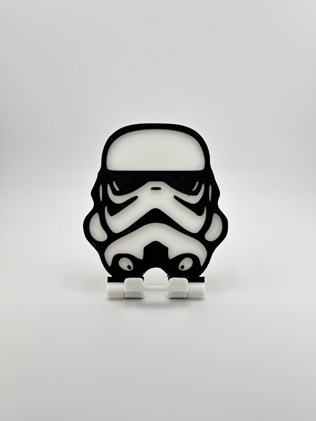 Compact foldable phone stand with a black and white Stormtrooper design, inspired by Star Wars, ideal for supporting smartphones and small tablets.