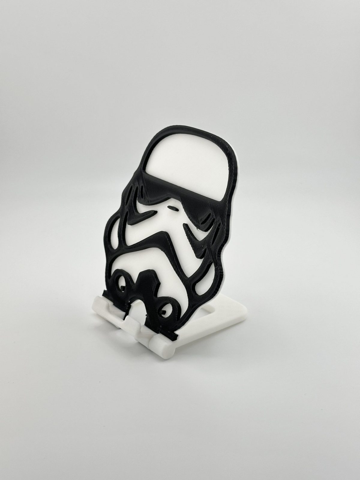 Compact foldable phone stand with a black and white Stormtrooper design, inspired by Star Wars, ideal for supporting smartphones and small tablets.