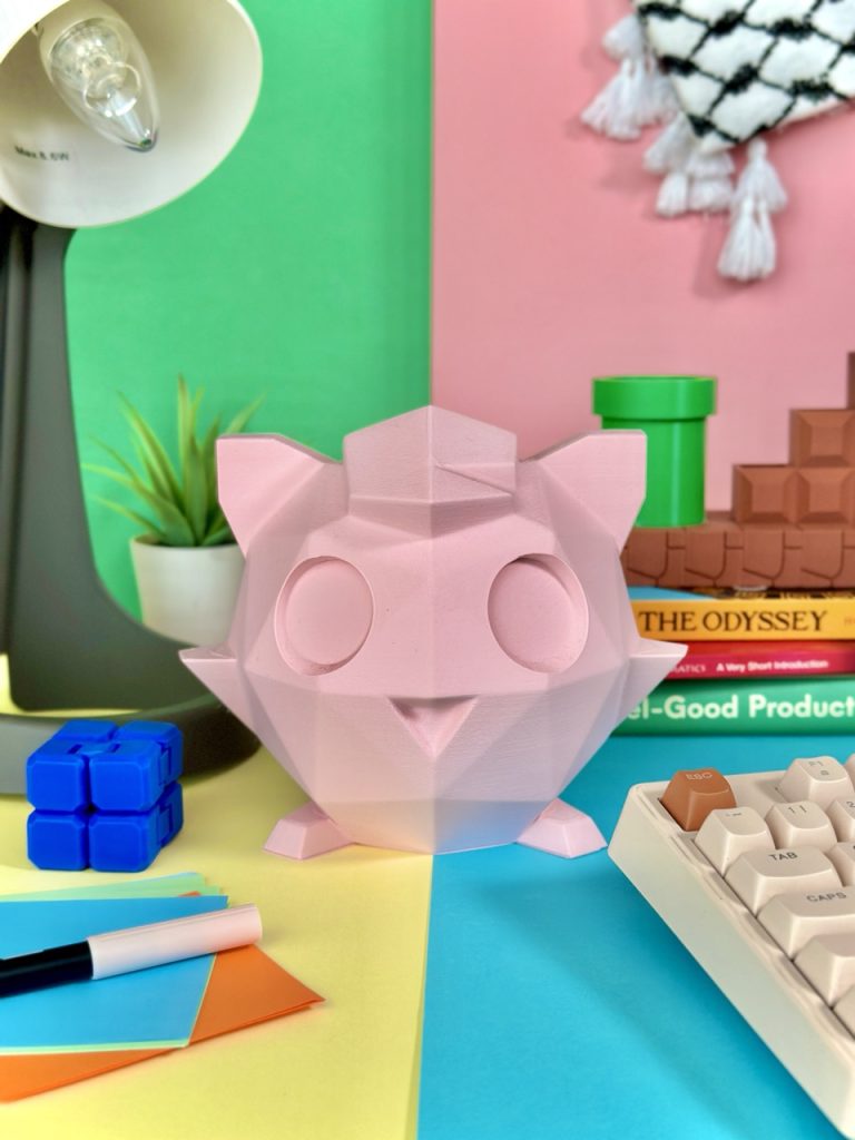 Matte light pink low-poly 3D-printed Jigglypuff coin bank, standing 15 cm tall with a coin slot, perfect for fans of the singing Pokémon.